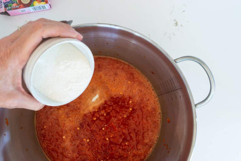 Pouring pectin and sugar into red pepper puree.