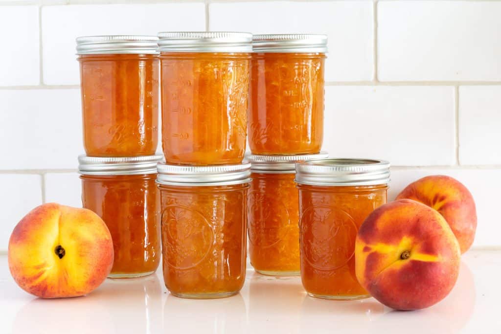 Jars of peach preserves with fresh peaches.