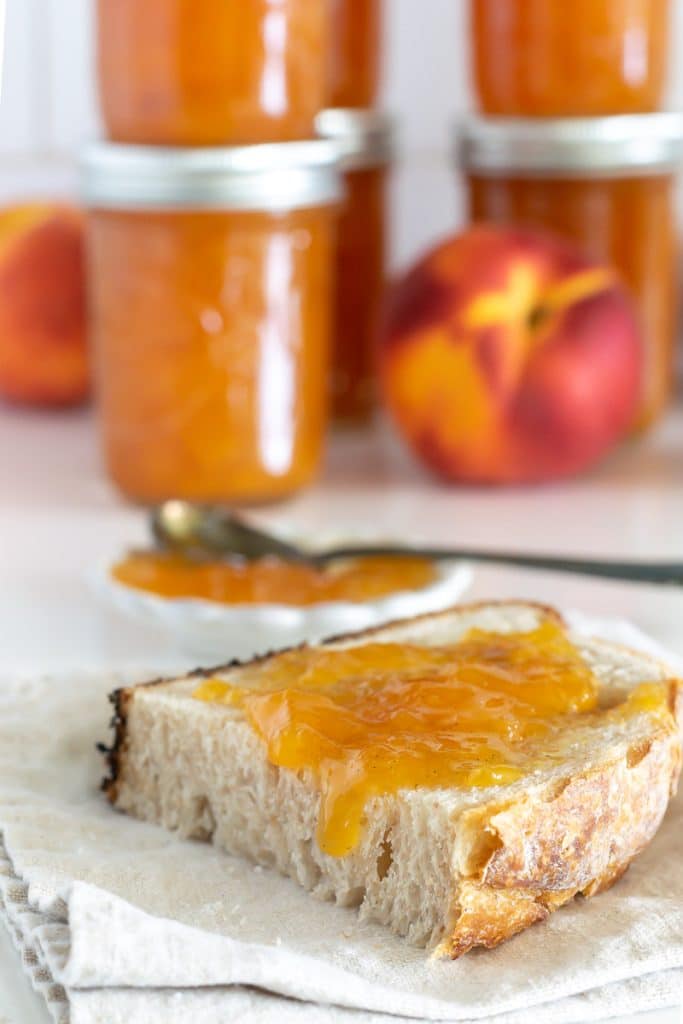 jars of peach preserves with preserves on a piece of bread.
