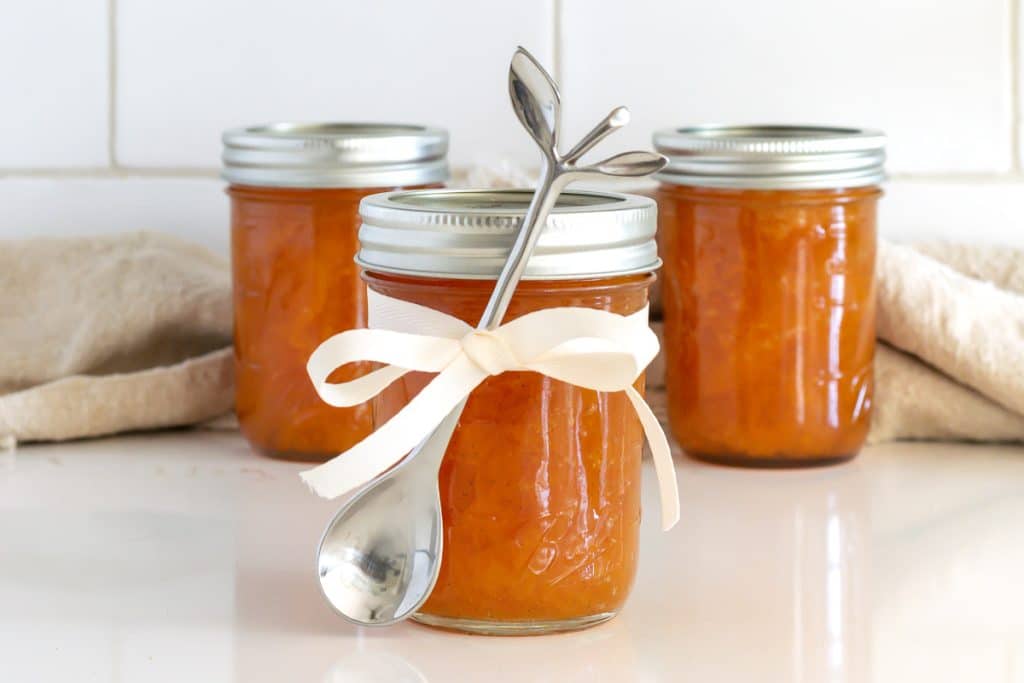Jar of peach preserves with a ribbon and a small spoon tied in the ribbon.