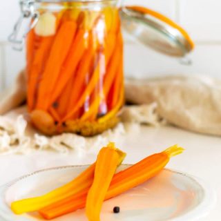 A jar of pickled carrots with a plate of pickled carrots in front.