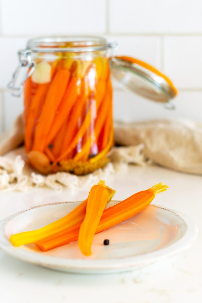 A jar of pickled carrots with a plate of pickled carrots in front.