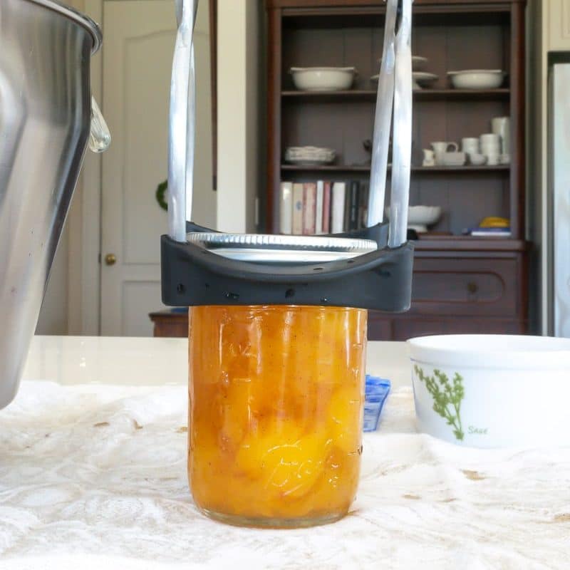 Use jar lifter to pick up jar of peach preserves to put it back in the pot of hot water.