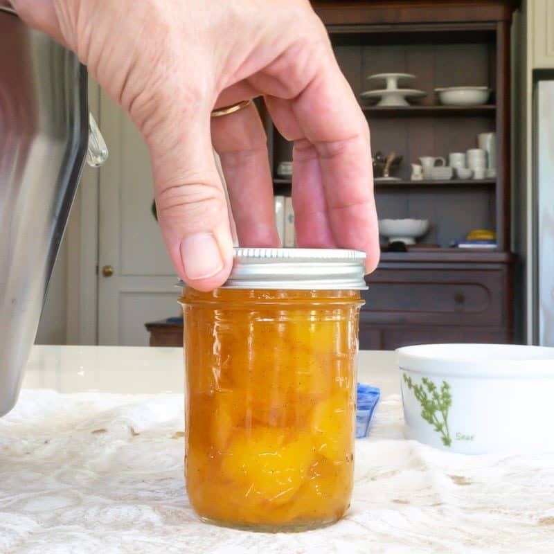 Screw lid on jar of peach preserves.