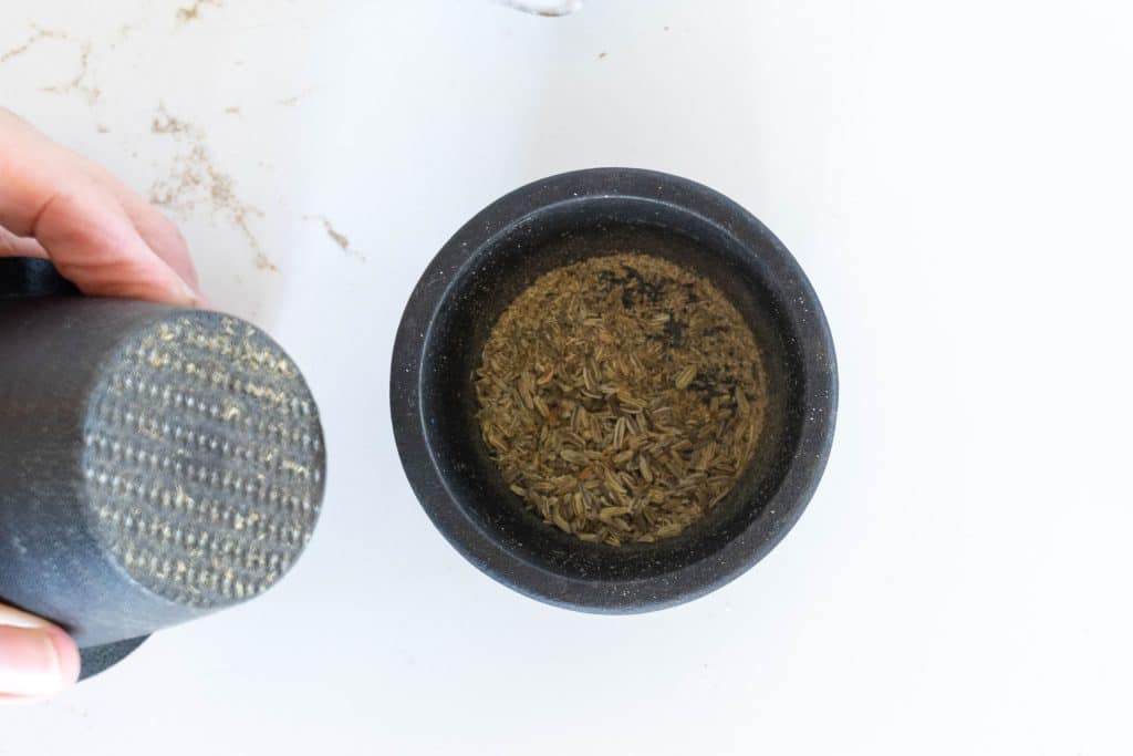 Crushed fennel seeds in cast iron spice grinder.