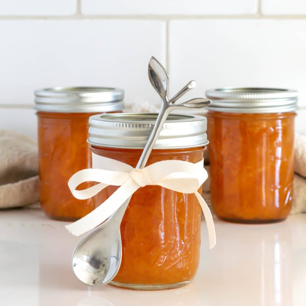 Peach preserves with spoon tied to jars with a ribbon.