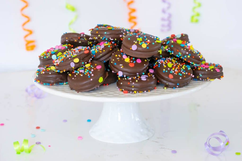 Chocolate Covered Oreos on a cake stand with ribbons and confetti in the background.