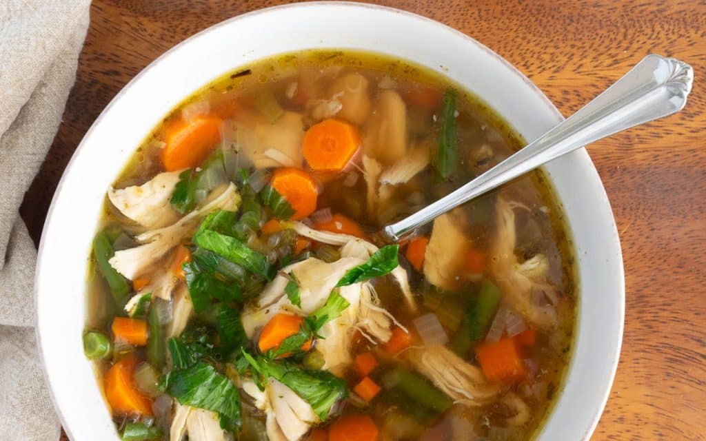 Bowl of chicken vegetable soup on a wooden tray.