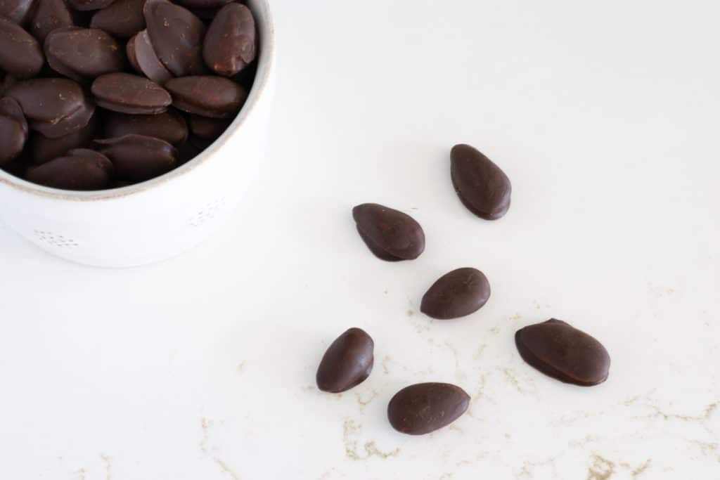 chocolate covered almonds in a bowl and on the counter.
