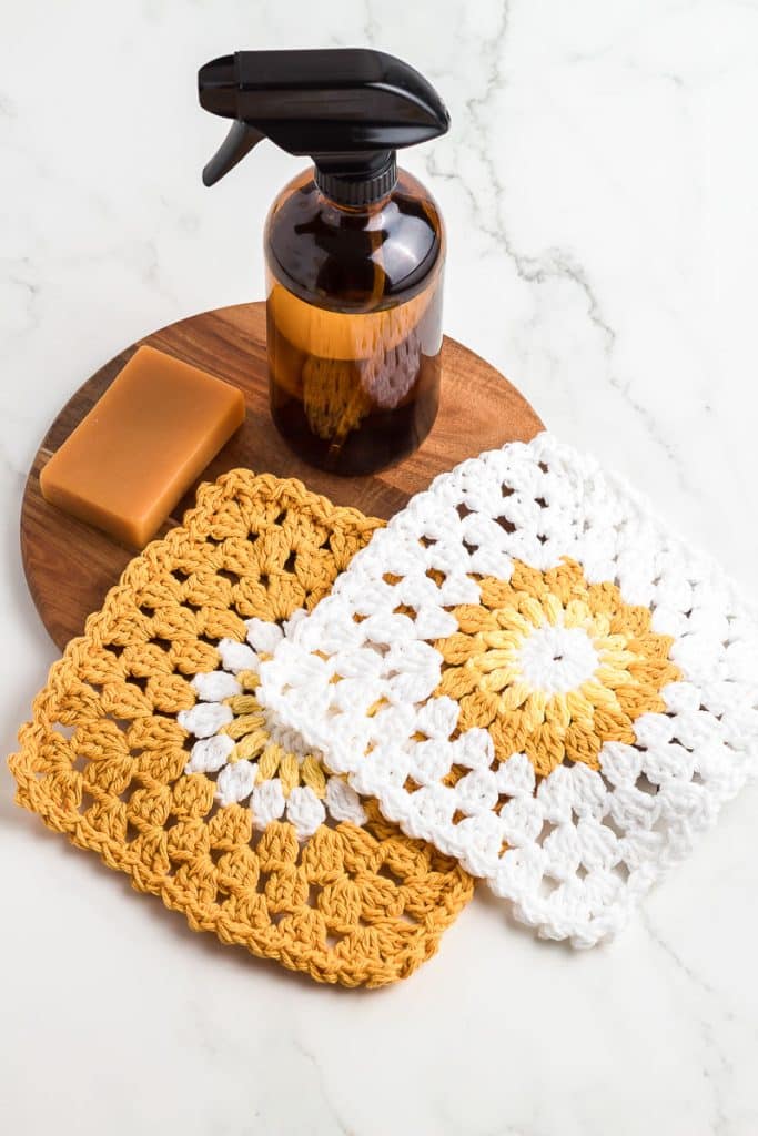 Two sunburst crochet dishcloths with a bar of soap and spray cleaner.