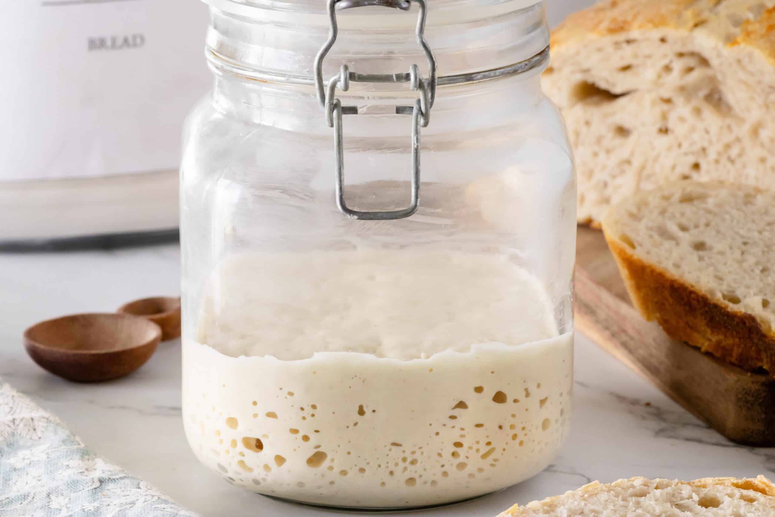 Sourdough Starter in a jar with a loaf of bread in the background.