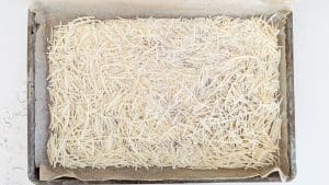 Shredded parmesan cheese over parchment paper on baking tray.