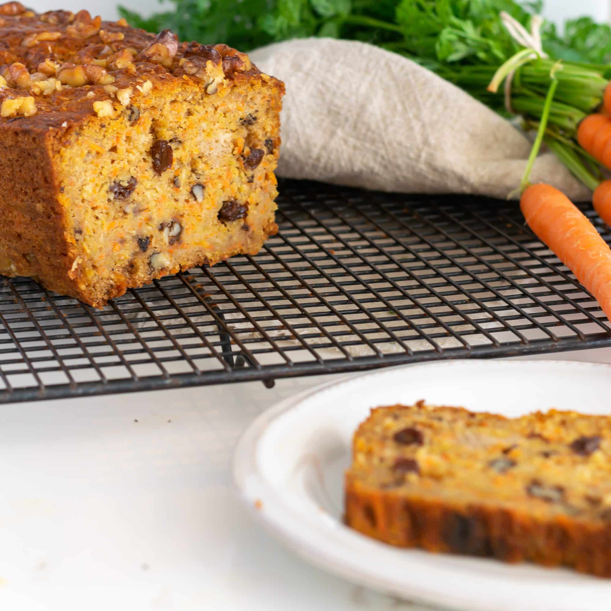 Carrot bread loaf on a cooling rack with fresh carrot in the background.