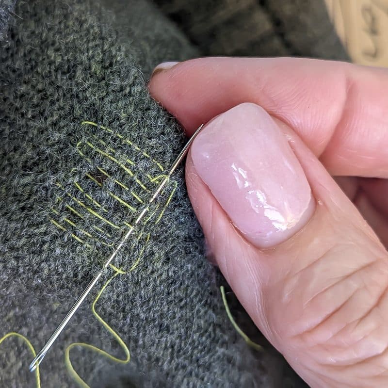 Using needle and thread to mend a hole in knit fabric.