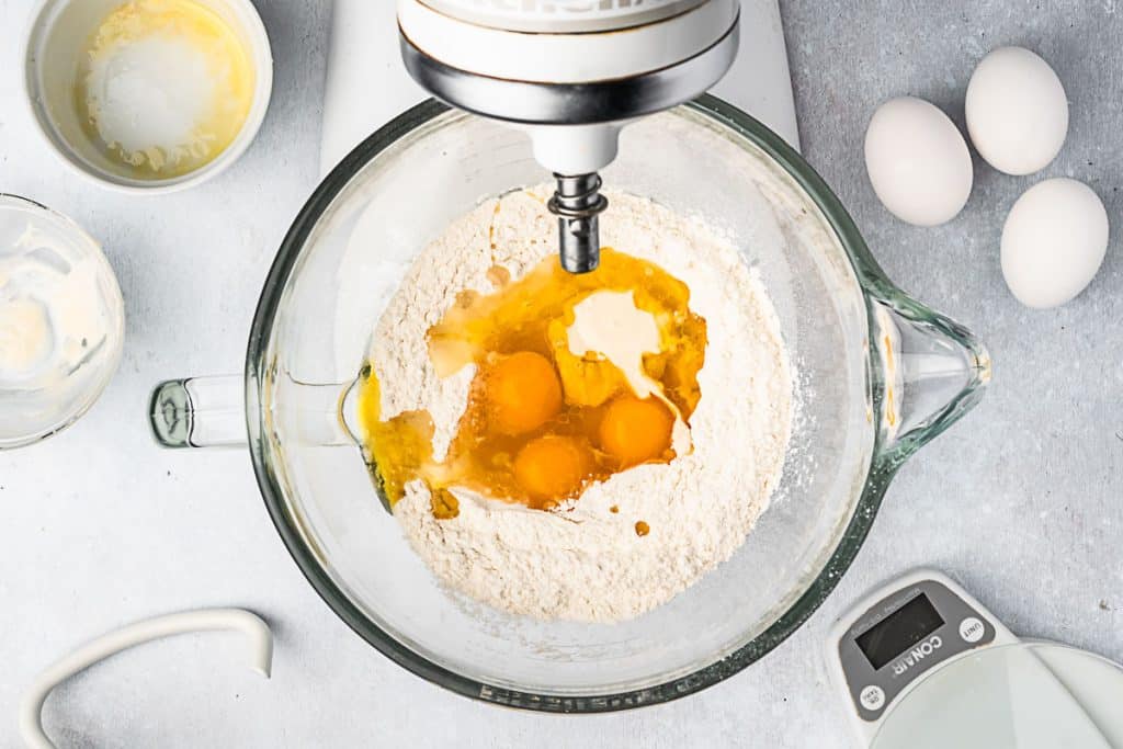 Eggs, oil and sourdough starter added to flour in mixing bowl.