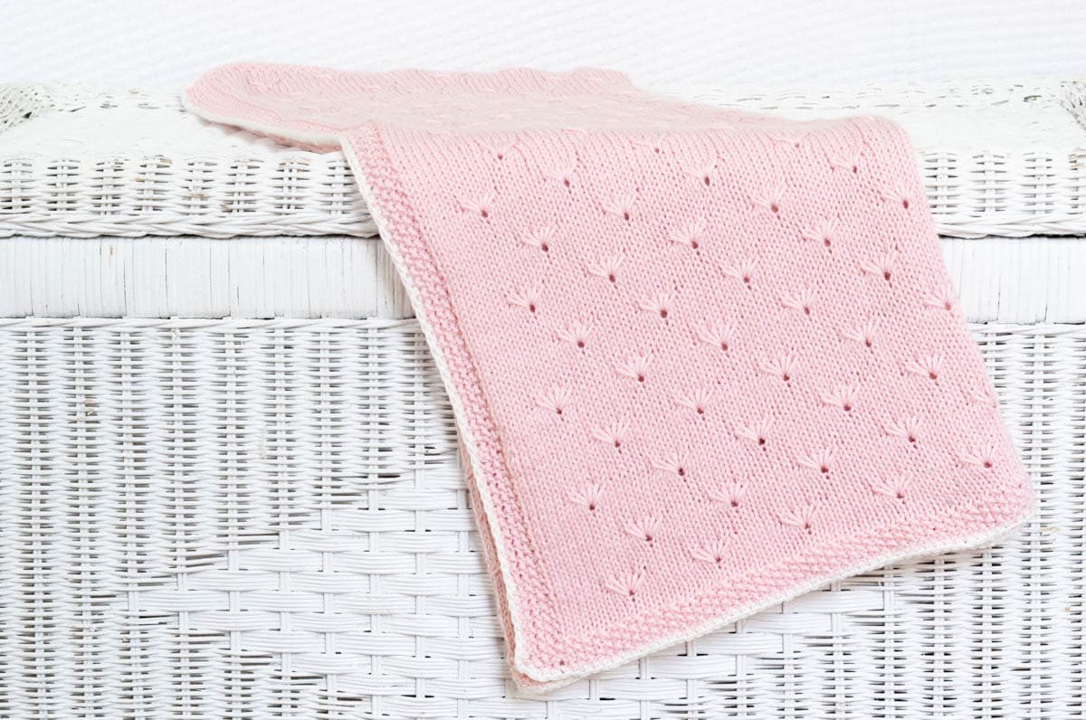 Finished pink dandelion baby blanket on white wicker chest.