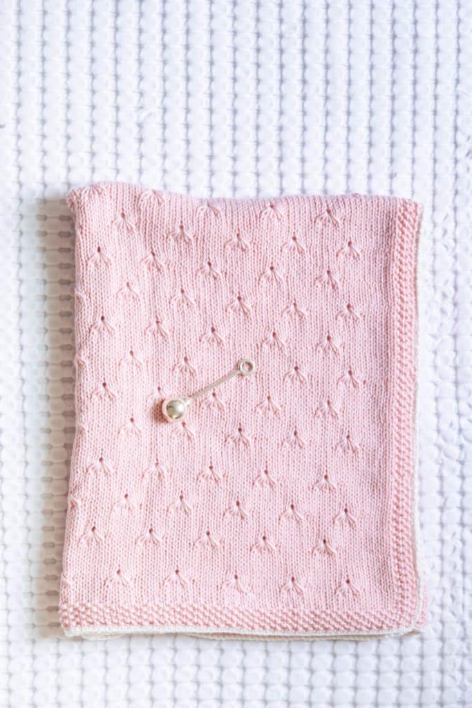 Finished pink dandelion baby blanket on white wicker chest.